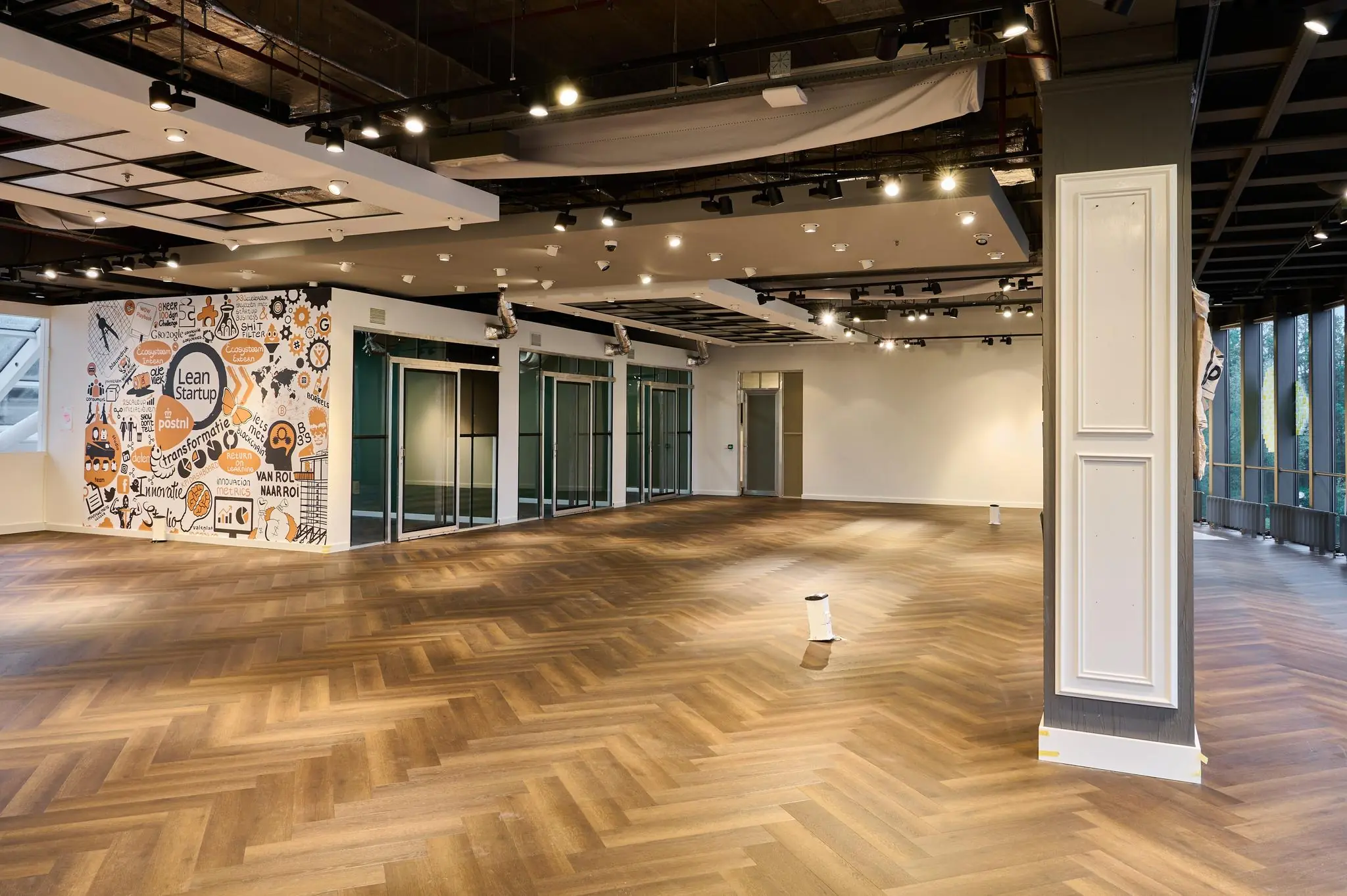 Ruime, modern ingerichte kantoorruimte aan de Johan Huizingalaan met houten visgraatvloer en een kleurrijke Lean Startup-muurillustratie.